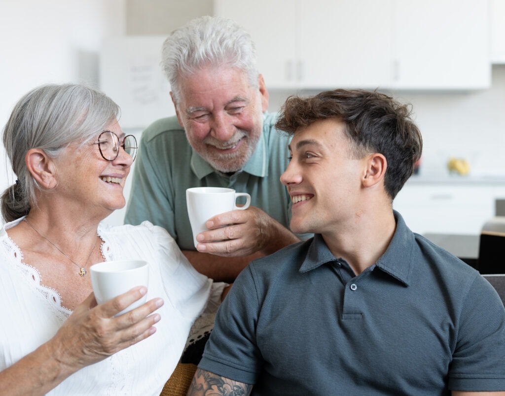 Avós e neto em conversa descontraída em casa, a tomar café, expressões de alegria genuína.